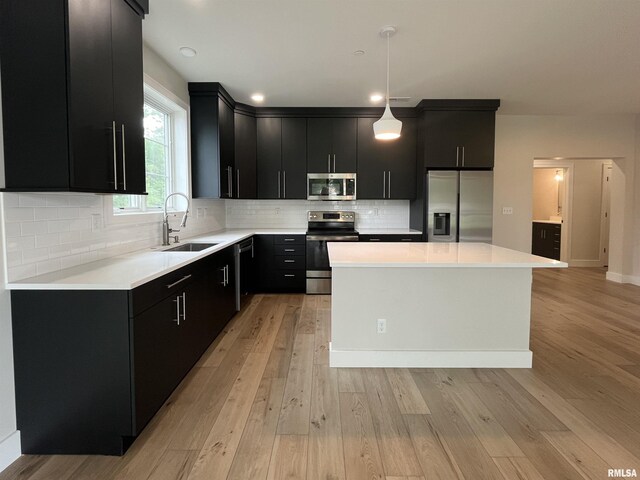 kitchen featuring stainless steel appliances, hanging light fixtures, light wood-type flooring, sink, and tasteful backsplash