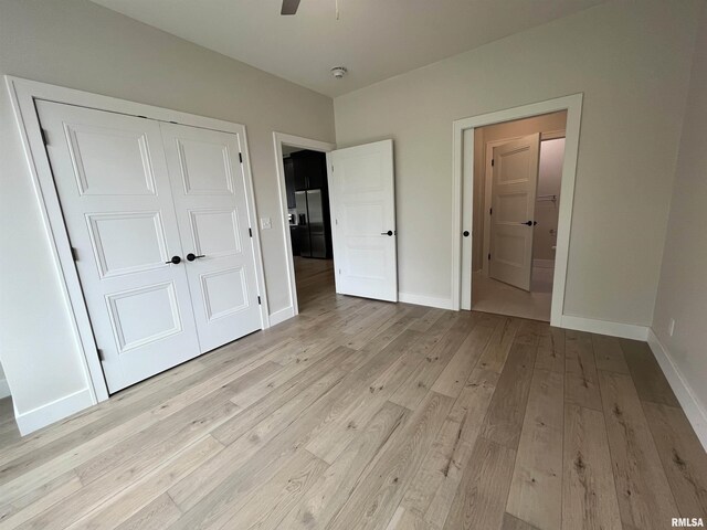 unfurnished bedroom with light wood-type flooring, black fridge with ice dispenser, and a closet