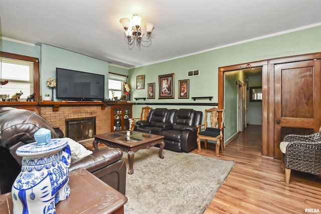 living room with a brick fireplace, a chandelier, ornamental molding, and light wood-type flooring