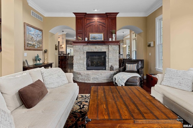 living area with wood finished floors, a stone fireplace, arched walkways, ornamental molding, and visible vents
