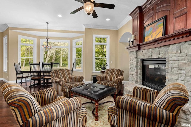 interior space with baseboards, ceiling fan with notable chandelier, wood finished floors, crown molding, and a fireplace