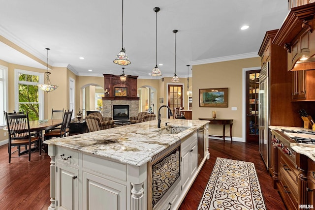 kitchen with arched walkways, a sink, baseboards, a stone fireplace, and dark wood-type flooring