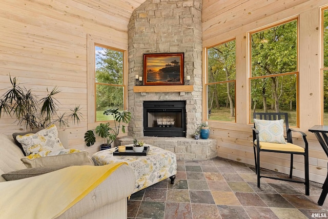 living room with stone tile floors, wooden walls, a stone fireplace, and high vaulted ceiling