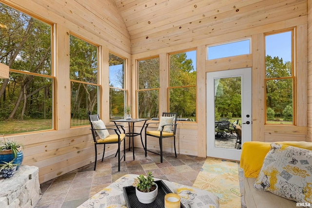 sunroom / solarium featuring stone finish flooring, vaulted ceiling, wood walls, and plenty of natural light