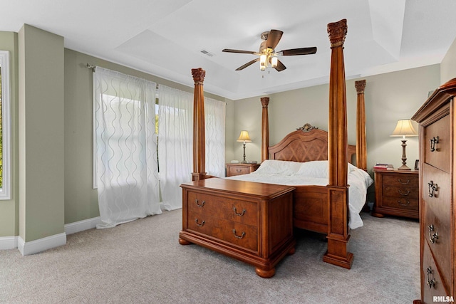 carpeted bedroom with a raised ceiling, visible vents, baseboards, and ceiling fan