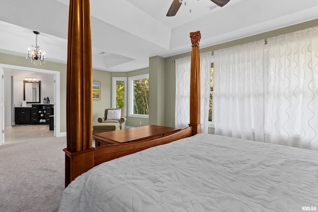 carpeted bedroom with decorative columns, visible vents, ceiling fan with notable chandelier, ensuite bath, and a raised ceiling