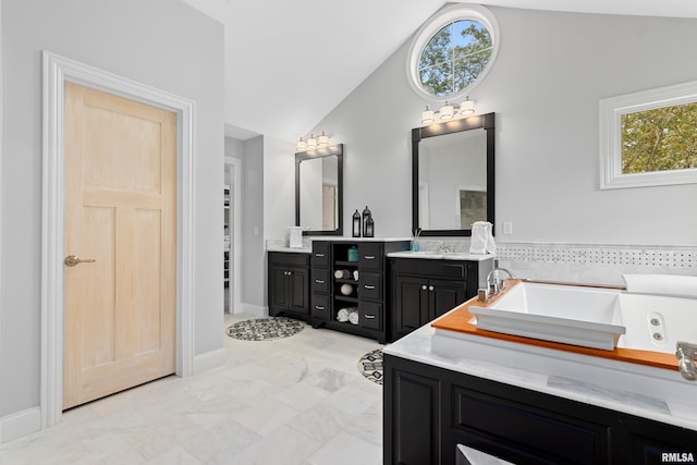 bathroom with baseboards, lofted ceiling, vanity, and a jetted tub