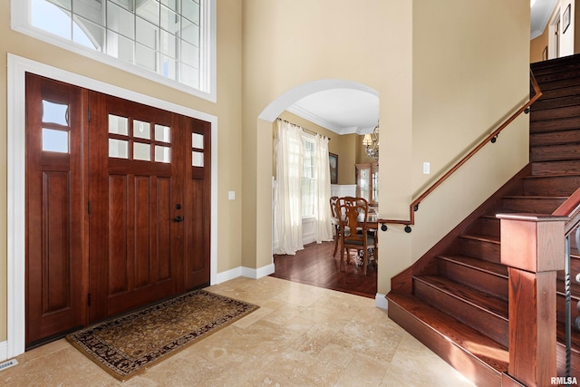 entryway featuring stairway, a high ceiling, a healthy amount of sunlight, arched walkways, and crown molding