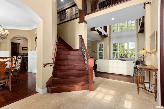 staircase with crown molding, arched walkways, an inviting chandelier, a towering ceiling, and visible vents