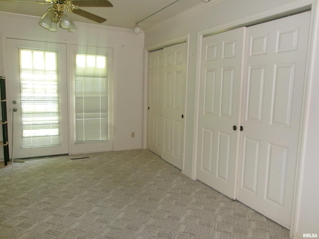 unfurnished bedroom featuring light carpet, multiple windows, crown molding, and two closets