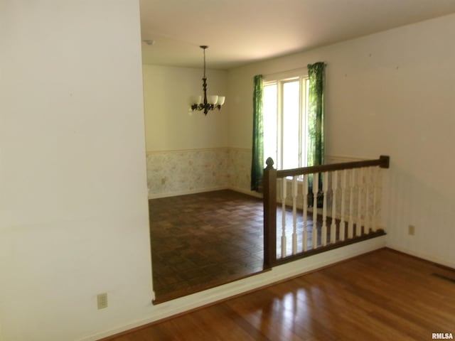 empty room with hardwood / wood-style floors and an inviting chandelier