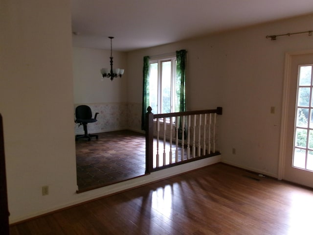 unfurnished dining area featuring a healthy amount of sunlight, an inviting chandelier, and dark hardwood / wood-style floors