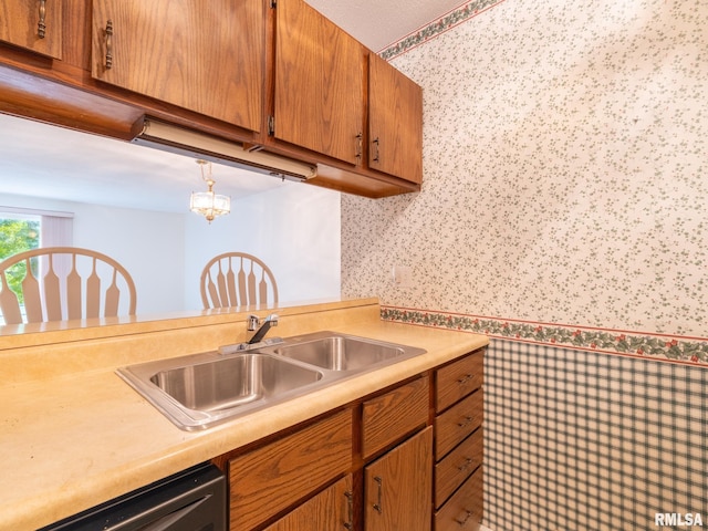 kitchen with dishwashing machine, brown cabinets, hanging light fixtures, light countertops, and a sink