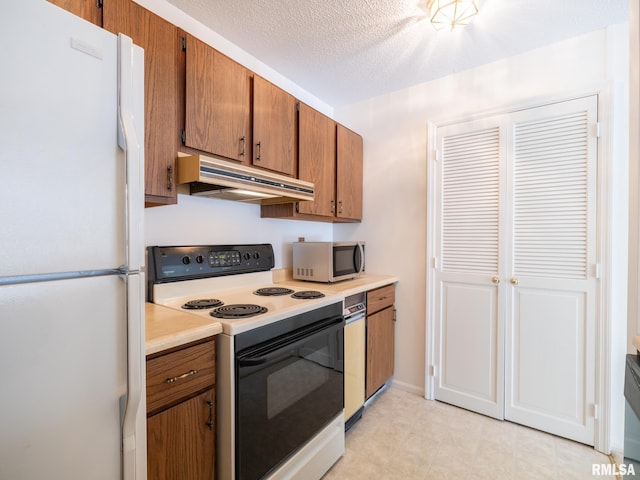 kitchen featuring stainless steel microwave, freestanding refrigerator, light countertops, under cabinet range hood, and range with electric stovetop