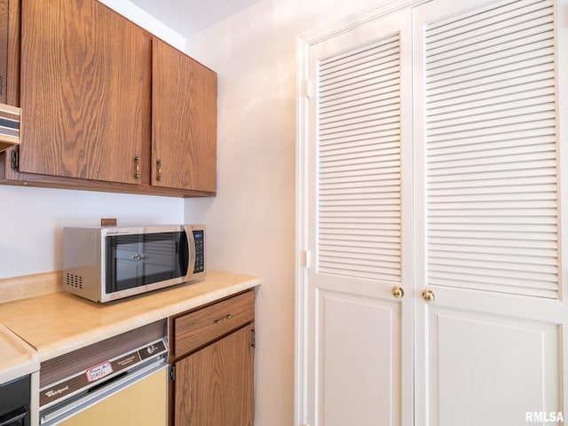 kitchen featuring dishwasher, light countertops, stainless steel microwave, and brown cabinetry