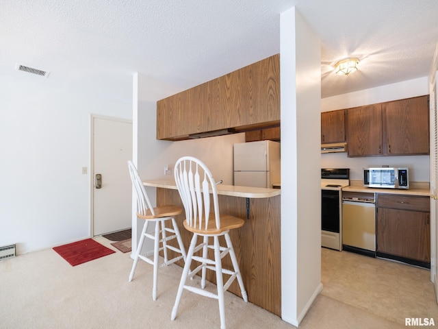 kitchen with light countertops, appliances with stainless steel finishes, a breakfast bar, and brown cabinets