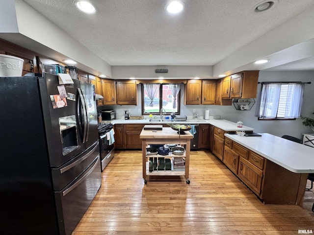 kitchen featuring gas range, light countertops, a peninsula, and black fridge