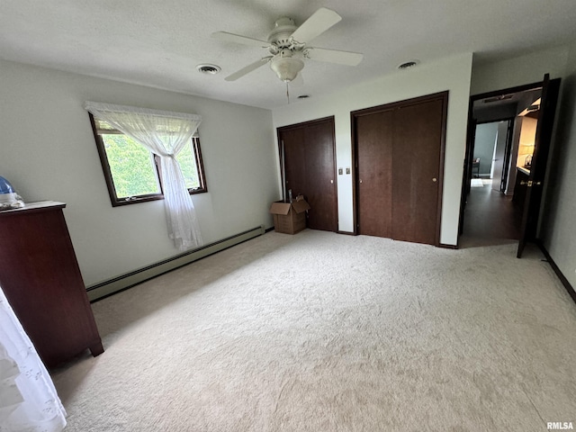 unfurnished bedroom featuring visible vents, two closets, carpet flooring, a baseboard radiator, and ceiling fan