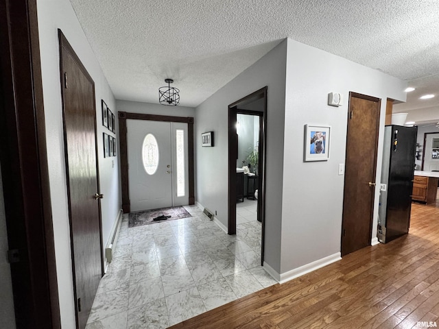 foyer entrance with light wood-style flooring, a textured ceiling, baseboards, and a baseboard radiator