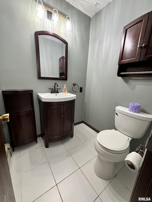 half bathroom featuring baseboards, toilet, vanity, tile patterned floors, and a textured ceiling