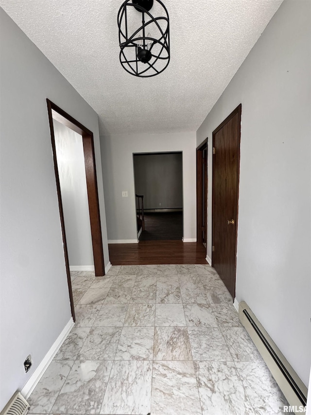 hallway with visible vents, marble finish floor, a textured ceiling, a baseboard radiator, and baseboards