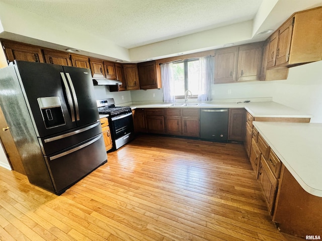 kitchen featuring under cabinet range hood, light wood-style flooring, appliances with stainless steel finishes, a textured ceiling, and a sink