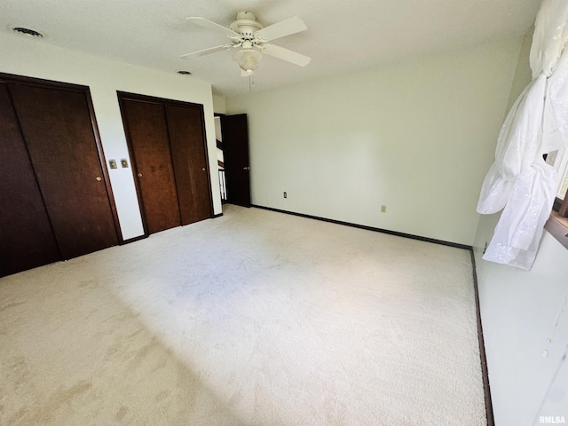 unfurnished bedroom featuring a ceiling fan, carpet, multiple closets, and baseboards