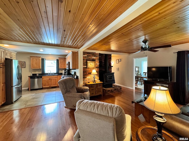 living room with wood ceiling, a wood stove, sink, light wood-type flooring, and ceiling fan