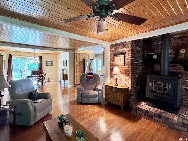 living room featuring ceiling fan, light wood-type flooring, a wood stove, and wooden ceiling