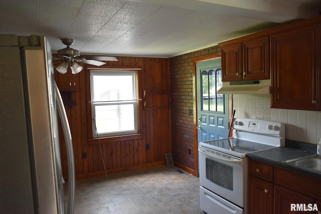 kitchen with white electric range, wall chimney exhaust hood, stainless steel refrigerator, and a wealth of natural light