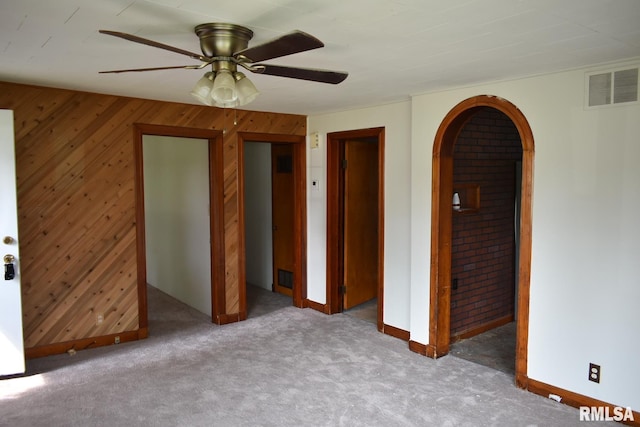 carpeted empty room featuring wooden walls and ceiling fan