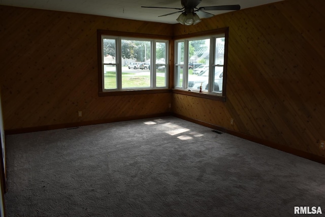 carpeted spare room with wooden walls and ceiling fan