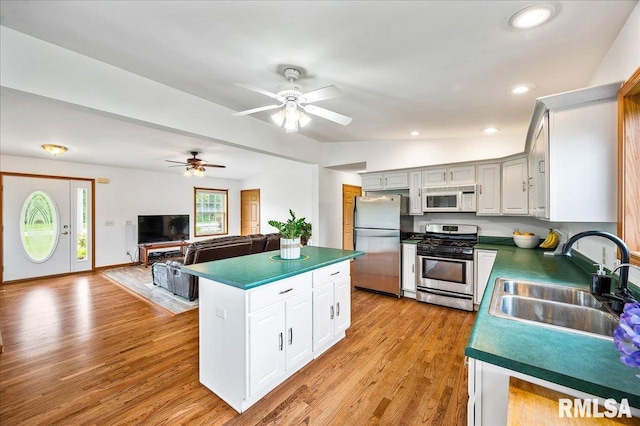 kitchen with stainless steel appliances, sink, white cabinets, and light hardwood / wood-style floors