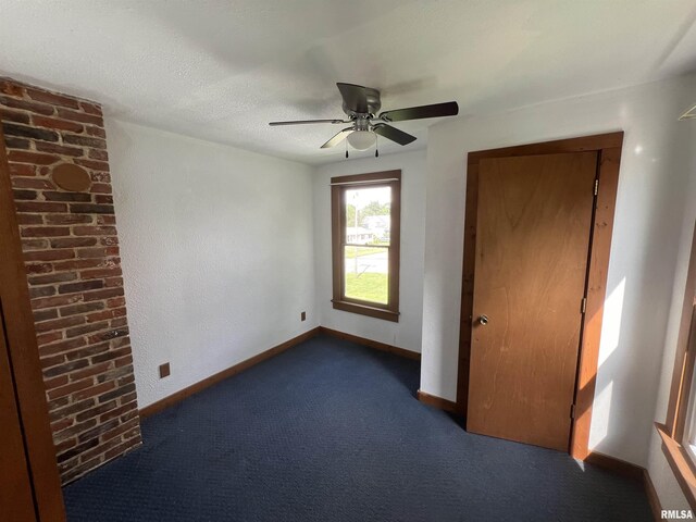 carpeted empty room with a textured ceiling, brick wall, and ceiling fan