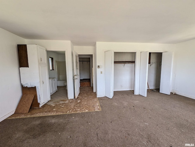 unfurnished bedroom with ensuite bathroom, carpet floors, and multiple closets