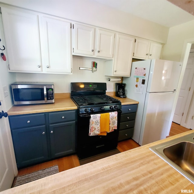 kitchen featuring hardwood / wood-style floors, sink, white cabinets, black range with gas stovetop, and white fridge