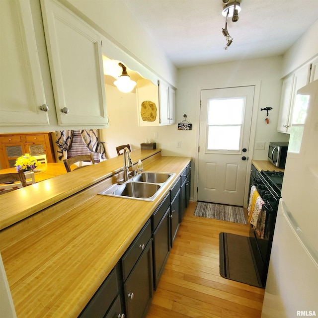 kitchen featuring sink, light hardwood / wood-style flooring, white cabinetry, black gas range, and white fridge