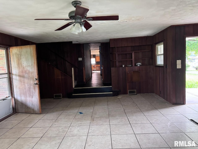 tiled entrance foyer with ceiling fan, a textured ceiling, and wooden walls