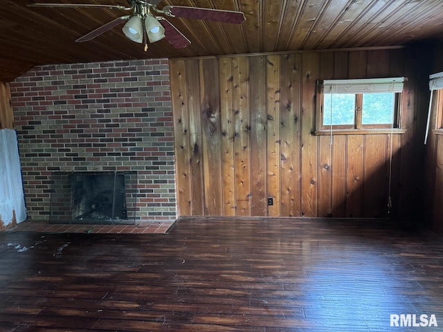 unfurnished living room with wood ceiling, dark wood-type flooring, a brick fireplace, ceiling fan, and wooden walls