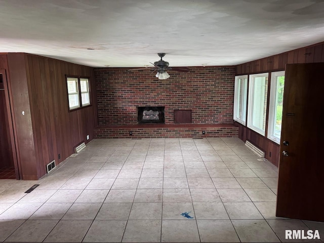 unfurnished living room featuring ceiling fan, light tile patterned floors, brick wall, wooden walls, and a fireplace