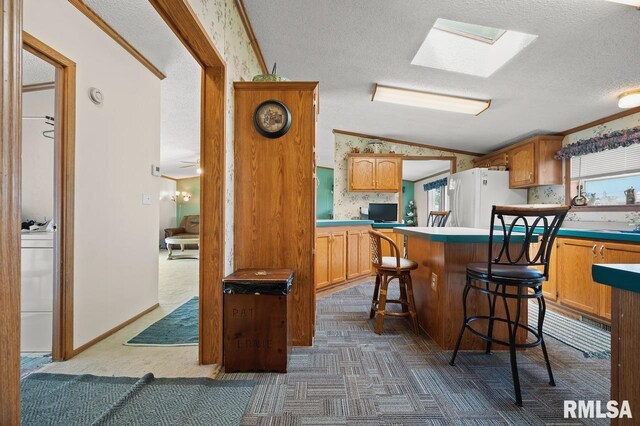 kitchen with a textured ceiling, vaulted ceiling with skylight, a kitchen island, freestanding refrigerator, and dark colored carpet