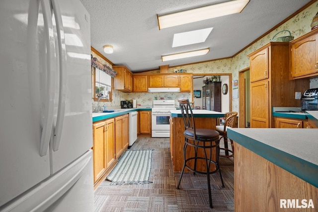 kitchen with a breakfast bar, vaulted ceiling with skylight, white appliances, tasteful backsplash, and a textured ceiling