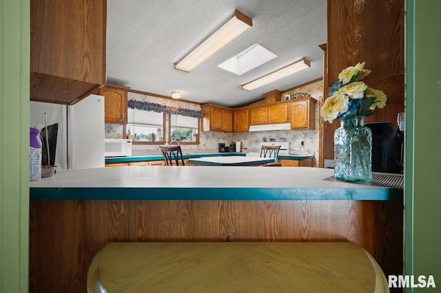 kitchen featuring vaulted ceiling with skylight, white appliances, tasteful backsplash, a textured ceiling, and kitchen peninsula