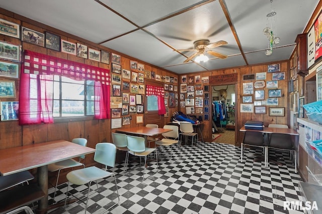 living area featuring tile patterned floors, wooden walls, and ceiling fan