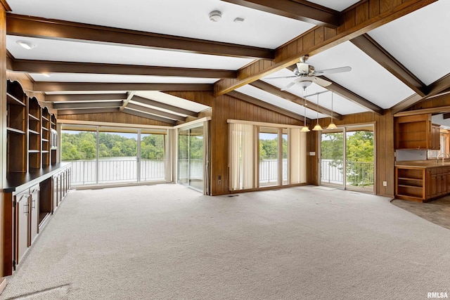 unfurnished living room featuring light colored carpet, wooden walls, lofted ceiling with beams, and ceiling fan