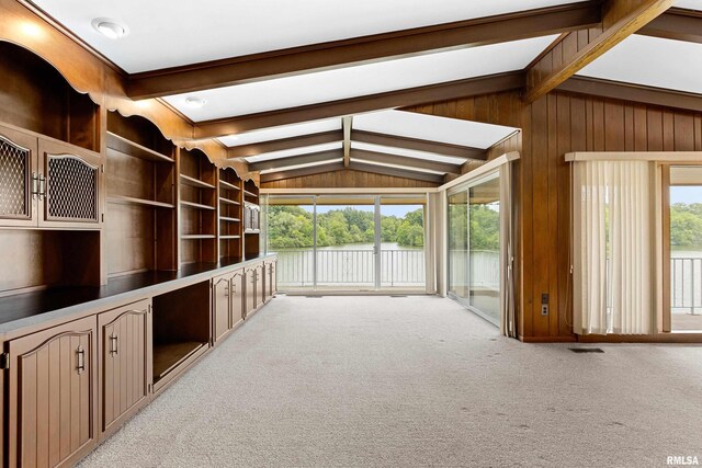 unfurnished living room featuring vaulted ceiling with beams, light colored carpet, and wooden walls