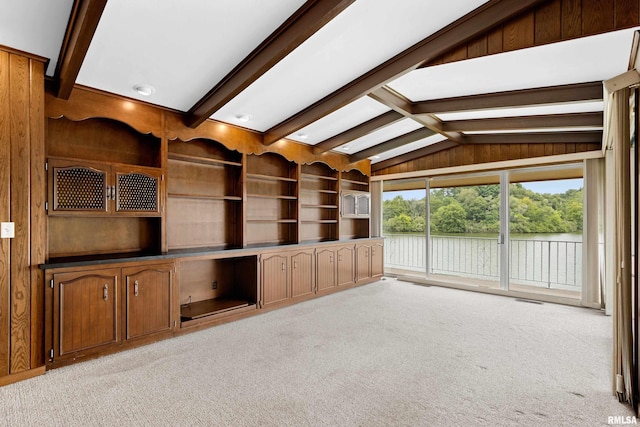 unfurnished living room with light colored carpet, built in features, lofted ceiling with beams, and wood walls