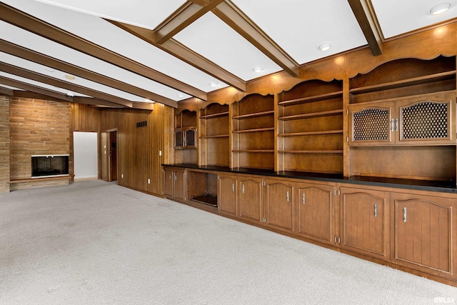 unfurnished living room featuring wooden walls, a large fireplace, light carpet, and beam ceiling