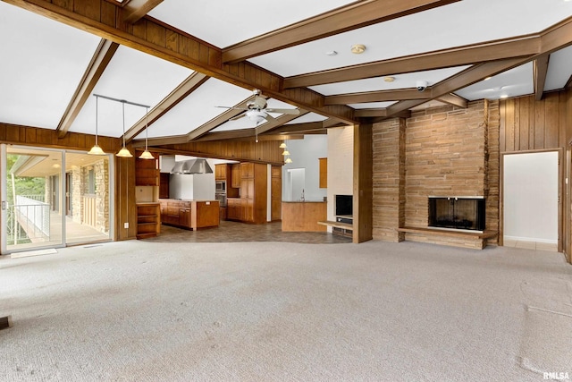 unfurnished living room featuring wood walls, high vaulted ceiling, beamed ceiling, a fireplace, and carpet