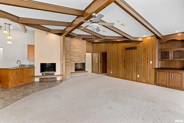 unfurnished living room with sink, ceiling fan, carpet flooring, a large fireplace, and wood walls